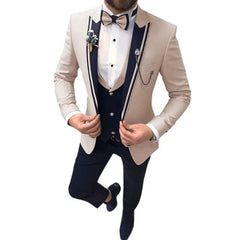 A man wears a beige three-piece suit with navy blue lapel accents, a matching vest, and trousers.