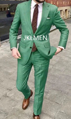 A man wears a green two-piece suit with a white shirt, patterned tie, and brown leather shoes.