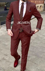 A man wears a slim-fit burgundy two-piece suit with a white shirt and a patterned tie.