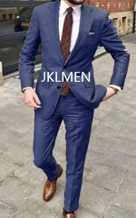 A man wears a blue two-piece suit with a patterned tie and brown leather shoes.