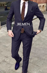 A man wears a dark navy blue two-piece suit with a patterned tie and blue dress shoes.