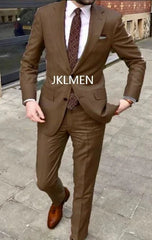 A man wears a brown two-piece suit with a white shirt and a patterned tie.