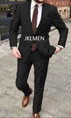 A man wears a black two-piece suit with a patterned tie and brown leather shoes.