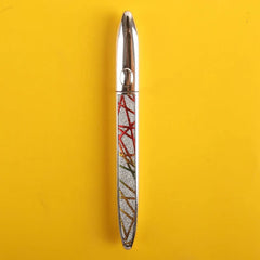 A silver eyeliner pen with a decorative, glittery geometric pattern on a yellow background.