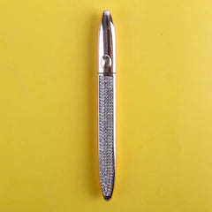 A rose gold eyeliner pen with a crystal-encrusted barrel on a yellow background.