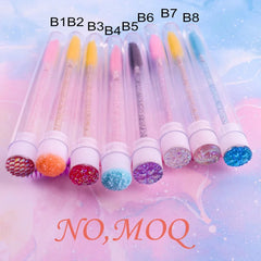 A row of colorful eyelash brushes in clear tubes with decorative, jeweled caps.