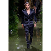 A model wears a navy blue silk satin suit featuring a shawl lapel jacket and a matching belt.