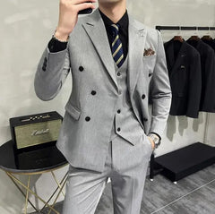 A man wears a grey three-piece slim-fit suit with a black shirt and a striped tie.