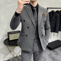 A man wears a grey double-breasted three-piece suit with a black shirt and patterned tie.