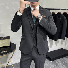 A man wears a charcoal grey three-piece slim-fit suit with a white shirt and green patterned tie.