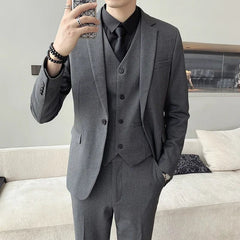 A man wears a charcoal grey three-piece suit with a black shirt and tie.