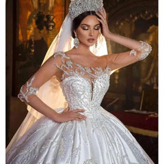 A woman wears a white ball gown wedding dress with long sleeves, beaded appliques, and a tiara.
