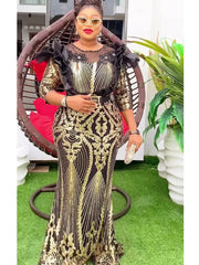 A woman wears a black and gold sequined maxi dress with ruffled shoulders and a belted waist.