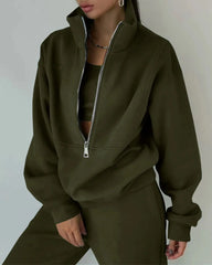 A woman wears an olive green two-piece tracksuit set featuring a zip-up collar and loose fit.