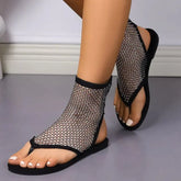 A pair of black flat gladiator sandals featuring a rhinestone-embellished mesh upper.
