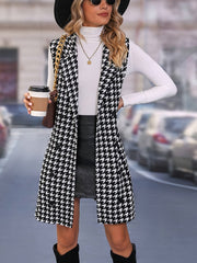 A woman wears a sleeveless, long houndstooth vest with a lapel collar over a white turtleneck.