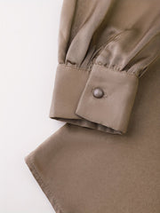 A close-up of a champagne-colored satin shirt sleeve featuring a buttoned cuff and gathered fabric.