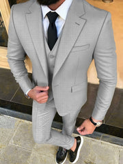 A man wears a light gray three-piece suit with a white shirt, black tie, and black loafers.