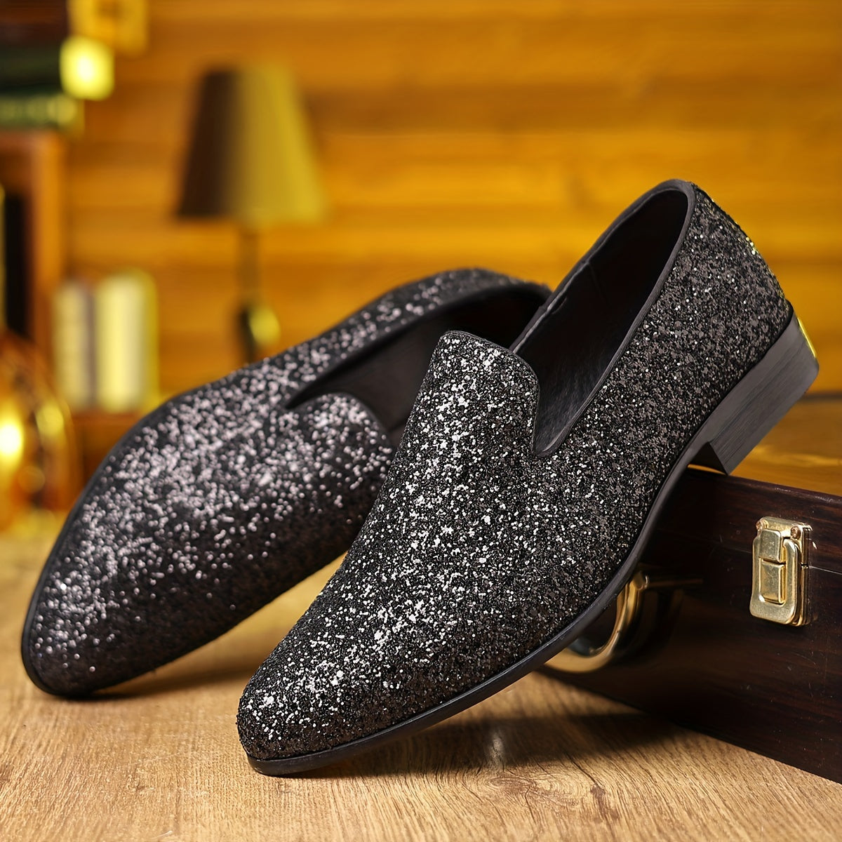 A pair of black glittery slip-on loafers with a pointed toe resting on a wooden surface.
