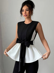 A woman wears a black and white sleeveless blouse featuring a round neck and a front bow tie.