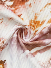 A close-up view of white fabric featuring a pleated texture and a brown and gold tie-dye pattern.