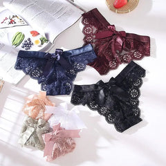 Three pairs of sexy lace thong underwear, each with a satin bow, are displayed on a white surface near a magazine and fruit. Product: 3 Pcs Woman Panties Sexy Lace Thong Underwear Lingerie Female T-back Low Waist Transparent G String.