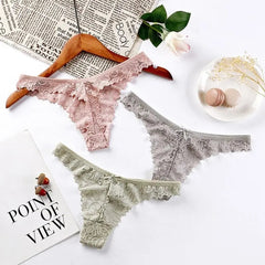 Three pairs of 3 Pcs Woman Panties Sexy Lace Thong Underwear in pink, gray, and light green are displayed on a white surface. One pair hangs on a wooden hanger beside a newspaper, rose, macarons, and a POINT OF VIEW page.