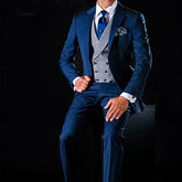 A man wears a blue three-piece suit with a grey double-breasted vest and a blue tie.
