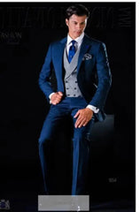 A man wears a blue three-piece suit with a grey double-breasted vest and a blue tie.