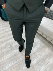 A man wearing a dark green three-piece suit with black loafers.