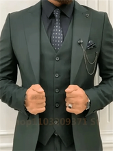 A man wears a dark green three-piece suit with a black shirt and patterned tie.