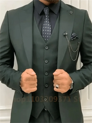 A man wears a dark green three-piece suit with a black shirt and patterned tie.
