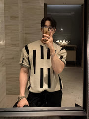 A man wears a cream-colored short-sleeve knitted sweater with a black vertical stripe pattern.