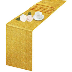 A gold sequin table runner draped over a surface with a teacup and flowers.