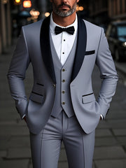 A man wears a light gray three-piece suit with a black shawl lapel and a black bow tie.