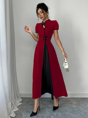 A woman wears a fitted, red, midi-length dress with a black V-neck, short sleeves, and a front slit.