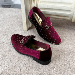 A pair of burgundy velvet slip-on loafers featuring gold-tone horsebit hardware and stud accents.