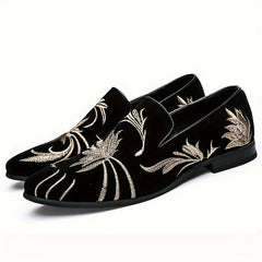 A pair of black velvet slip-on loafers featuring intricate gold floral embroidery and a pointed toe.