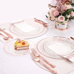 A rose gold dinnerware set featuring clear plates with metallic rims, cutlery, and napkins.