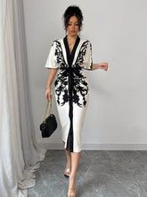 A woman wears a white midi dress with black floral prints, a V-neck, and a front tie waist.