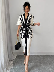 A woman wears a white midi dress with black floral prints, a V-neck, and a front tie waist.