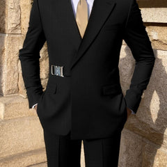 A man wears a black skinny-fit suit featuring a prominent silver metal belt detail at the waist.