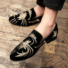 A pair of black slip-on loafers with gold floral embroidery and a pointed toe.