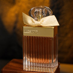 A rectangular glass perfume bottle with a gold cap, a decorative bow, and amber-colored liquid.
