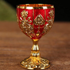 A small, vintage-style gold metal goblet with a red textured finish and embossed floral patterns.
