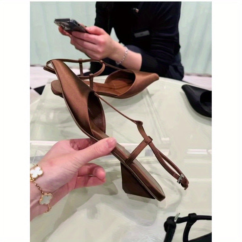 A pair of brown pointed-toe slingback sandals with a low chunky heel held in a hand.
