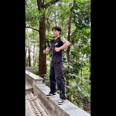 A person uses a black hydraulic chest expansion bar for upper body strength training outdoors.