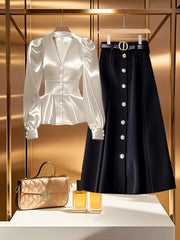 A white long-sleeve blouse with a v-neck and buttoned cuffs displayed next to a black midi skirt.