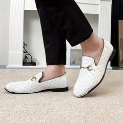 A pair of white slip-on loafers with gold-tone studs and a metal bit detail on a person.