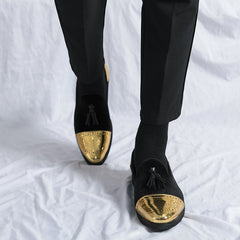 Black velvet loafers with gold metallic brogue toe caps and tassel details.